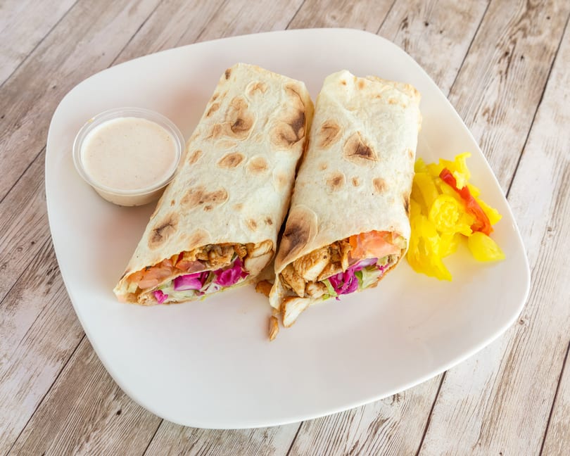 Two chicken shawarma wraps with sauce and pickled vegetables on a white plate.