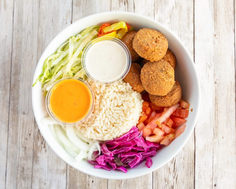 Falafel bowl with rice, lettuce, tomatoes, red cabbage, onions, and two sauces.