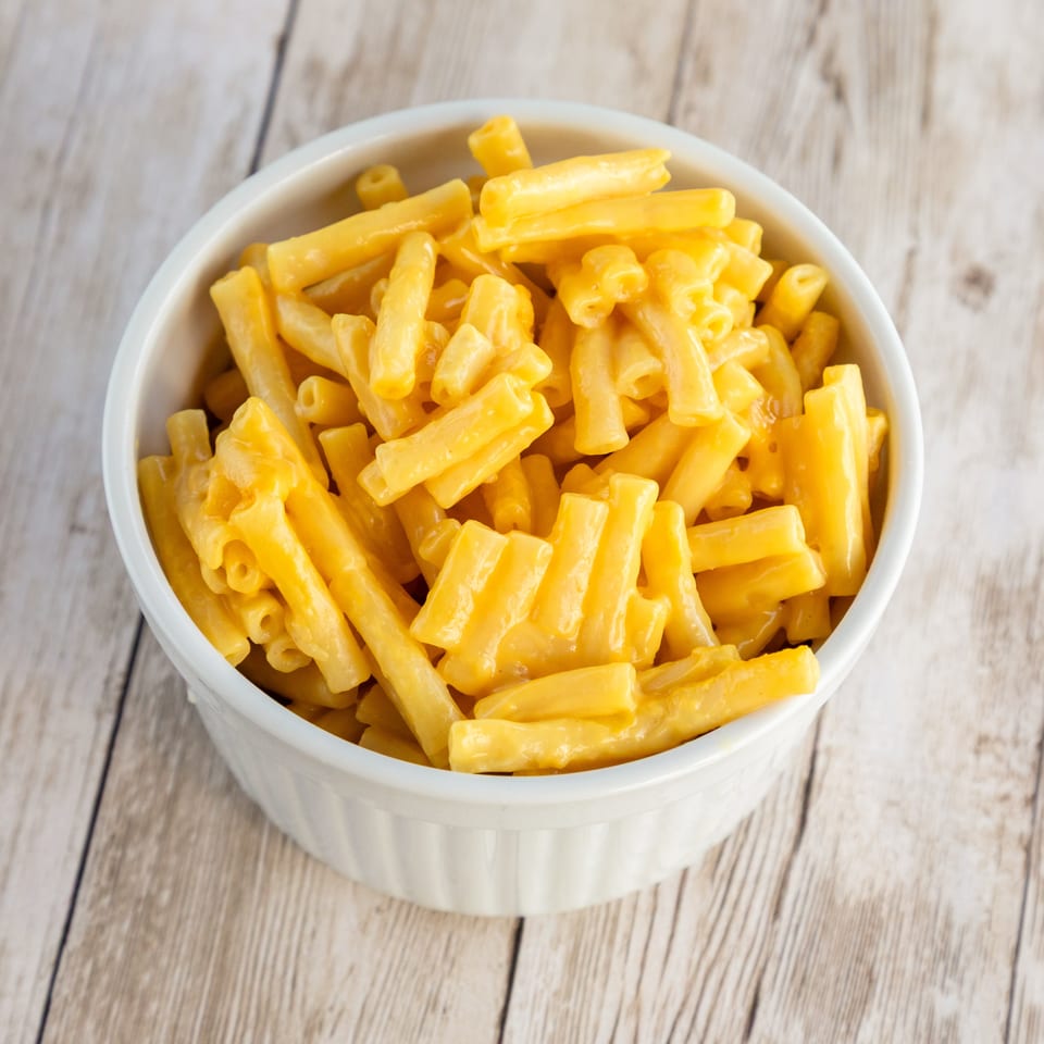 A white bowl filled with creamy, bright orange macaroni and cheese on a light wooden table.
