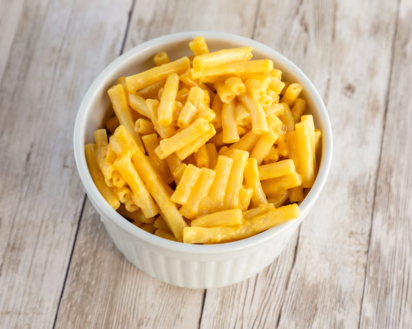 A white bowl filled with creamy, bright orange macaroni and cheese on a light wooden table.