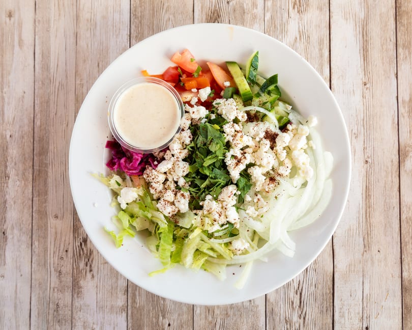 A fresh salad with lettuce, onions, tomatoes, cucumbers, feta cheese, and a side of dressing.