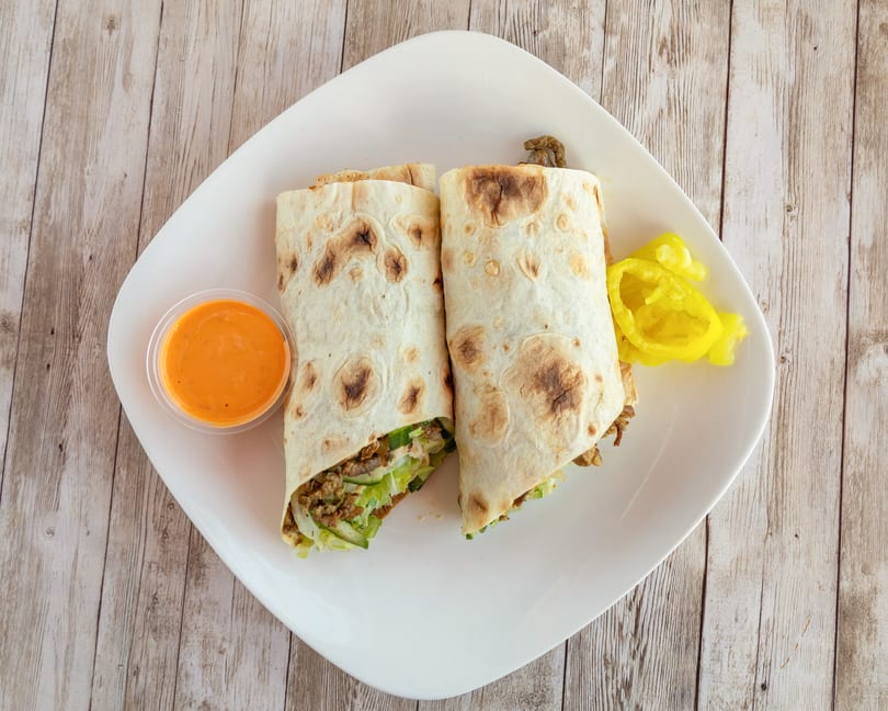 Two shawarma wraps with meat, lettuce, and onions, served with orange sauce and yellow peppers.