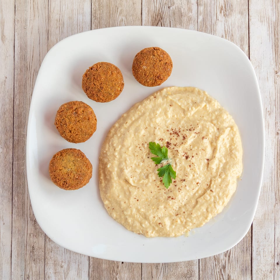 Four golden-brown falafel balls arranged around a swirl of hummus, garnished with parsley and paprika.