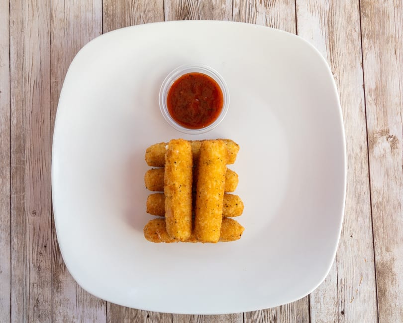 Golden-brown mozzarella sticks stacked on a white plate with a side of marinara sauce.