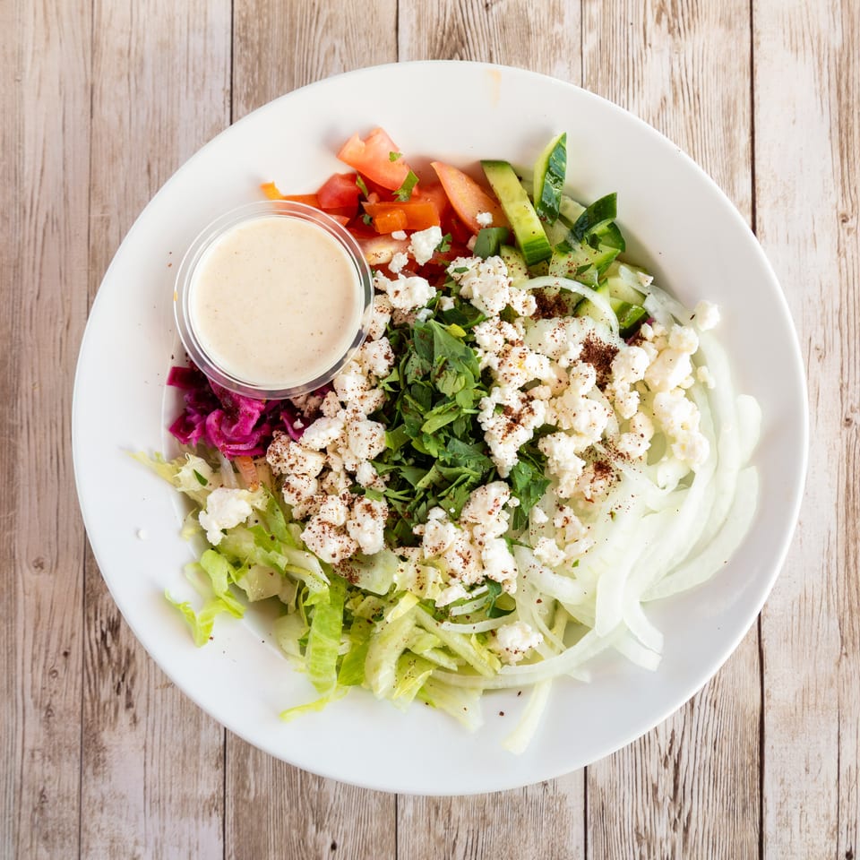 Overhead view of a fresh salad with lettuce, tomatoes, cucumbers, onions, feta, and dressing.