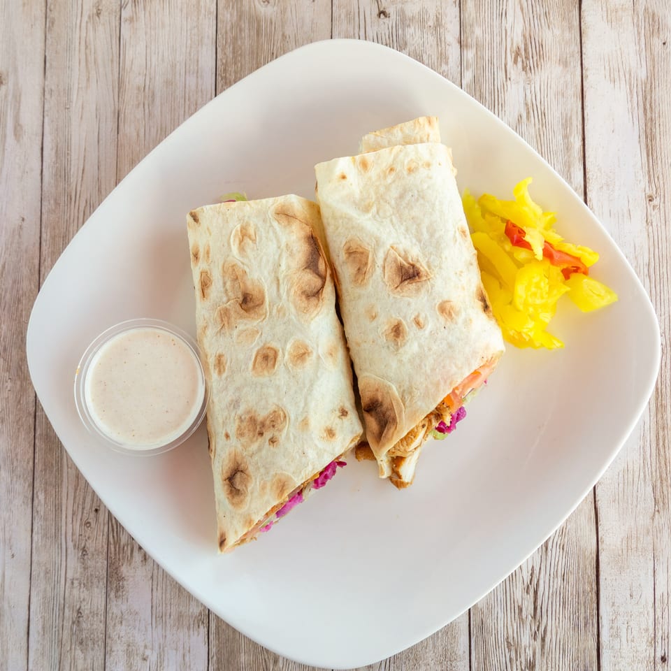 Two chicken shawarma wraps with a side of pickled vegetables and a dipping sauce on a white plate.