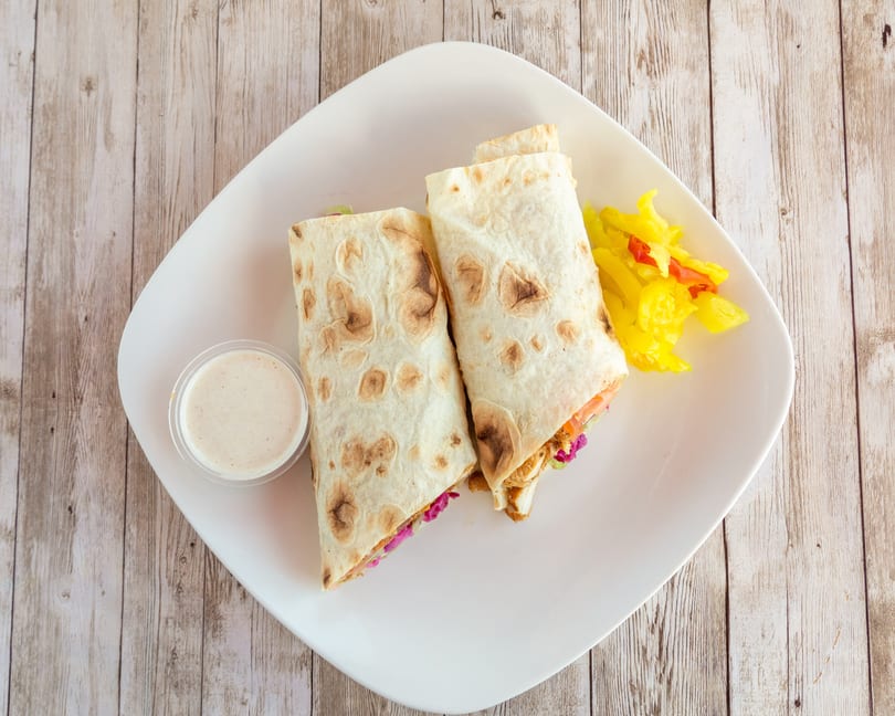 Two chicken shawarma wraps with a side of pickled vegetables and a dipping sauce on a white plate.