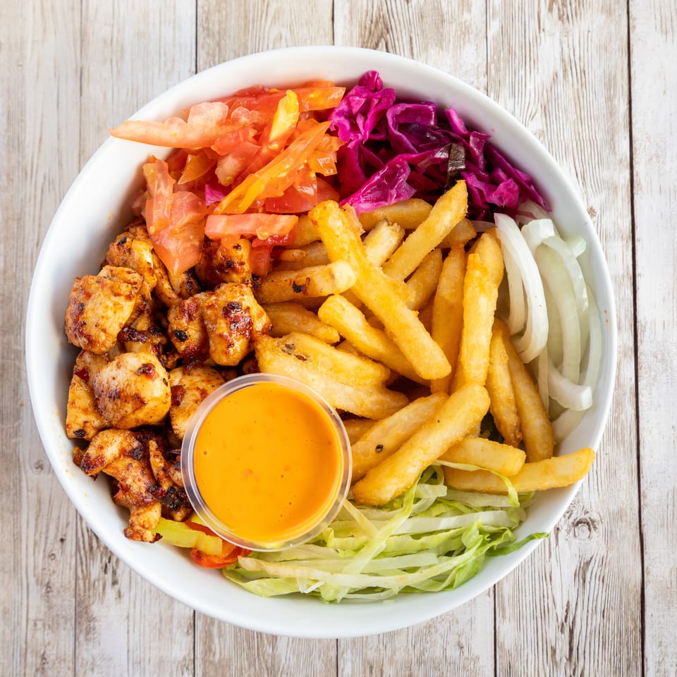 A white bowl filled with grilled chicken, french fries, red cabbage, tomatoes, onions, lettuce, and sauce.