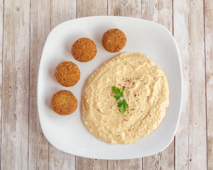 Four golden-brown falafel balls arranged around a swirl of hummus, garnished with parsley and spices.