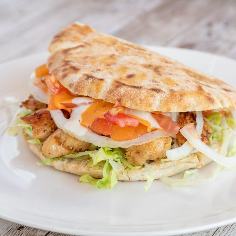 Chicken pita sandwich with lettuce, onions, tomatoes, and sauces on a white plate.