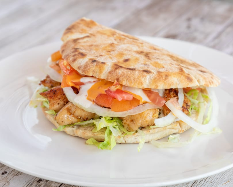 Chicken pita sandwich with lettuce, onions, tomatoes, and sauces on a white plate.