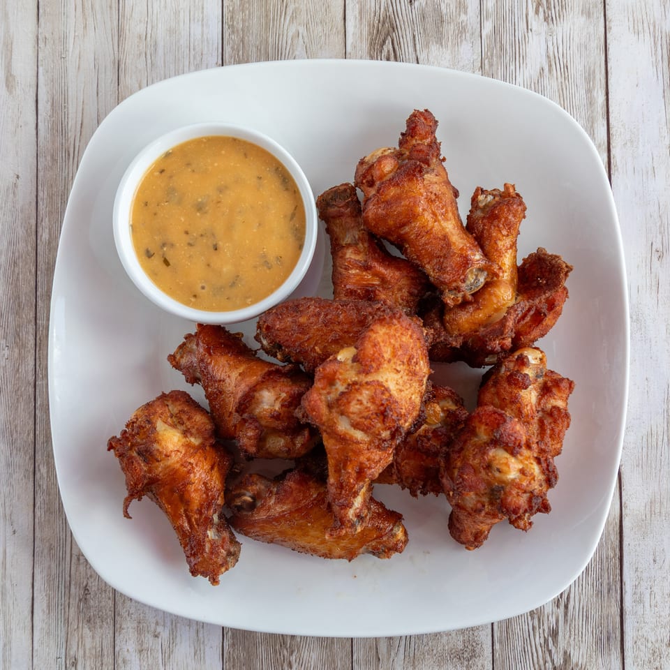 Crispy fried chicken wings and a small bowl of dipping sauce on a white plate.