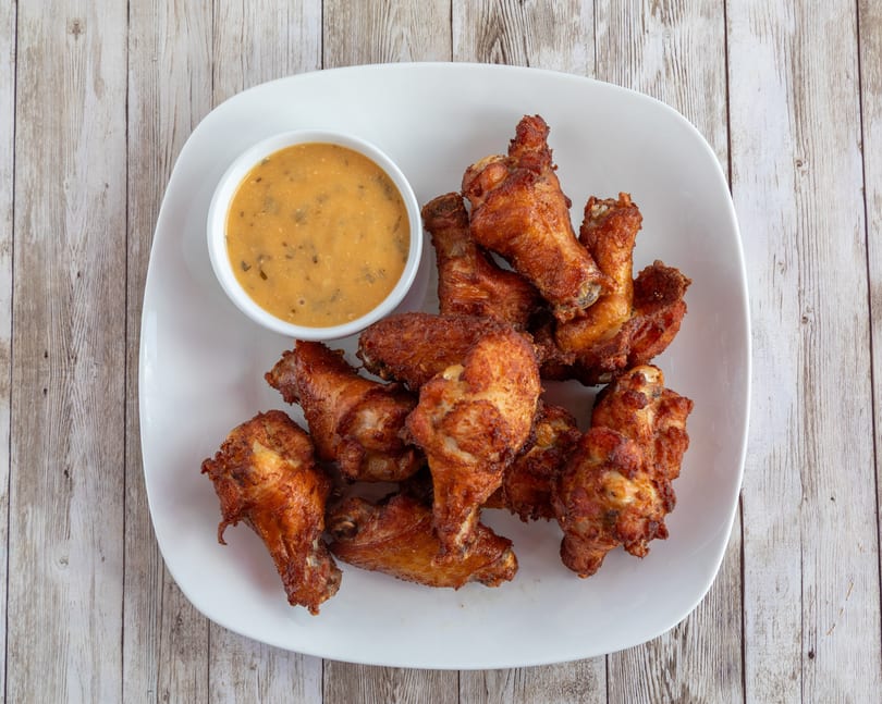 Crispy fried chicken wings and a small bowl of dipping sauce on a white plate.